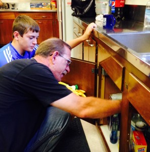 father son team working on plumbing in kitchen